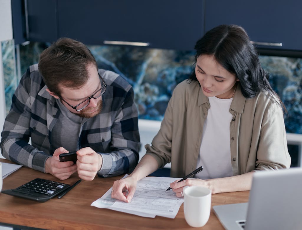 A couple reviewing financial documents at a table, using gadgets like a calculator and phone.